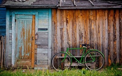 Stary drewniany budynek. Zielony rower jest o niego oparty